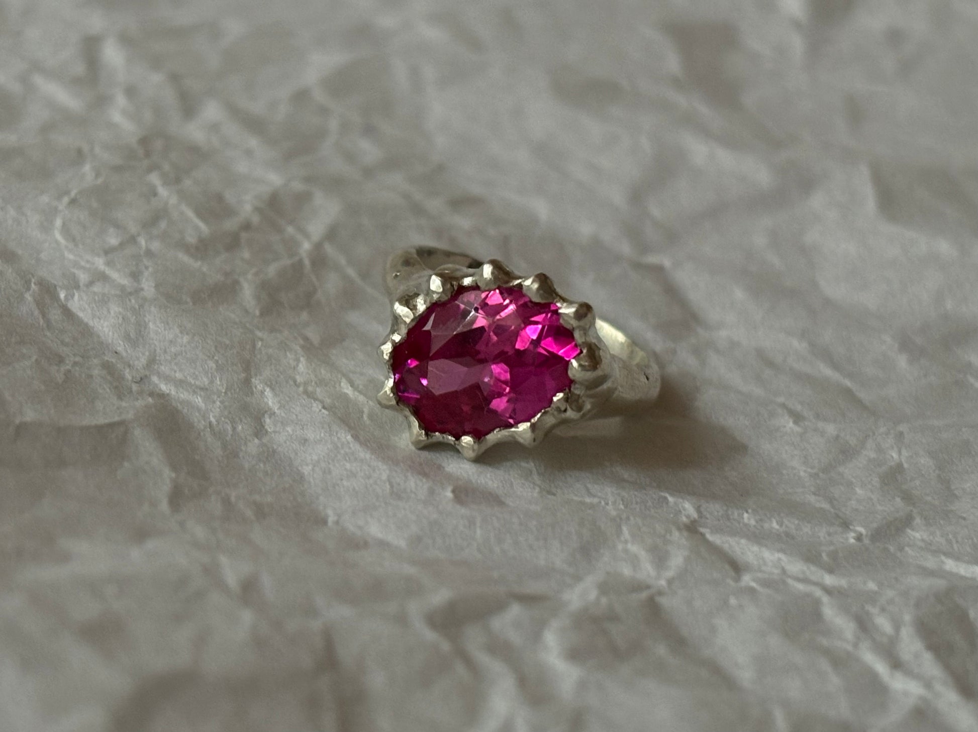 Silver ring with a pink gemstone on a textured white background